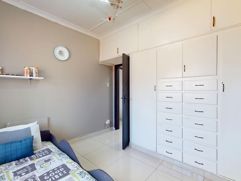 A bedroom featuring extensive built-in cabinetry with multiple drawers and overhead storage, complemented by neutral wall tones and tiled flooring.