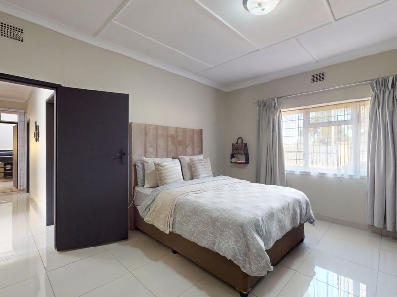A well-maintained bedroom featuring tiled flooring, a built-in cupboard, and a window with security bars, offering a clean and functional living space.