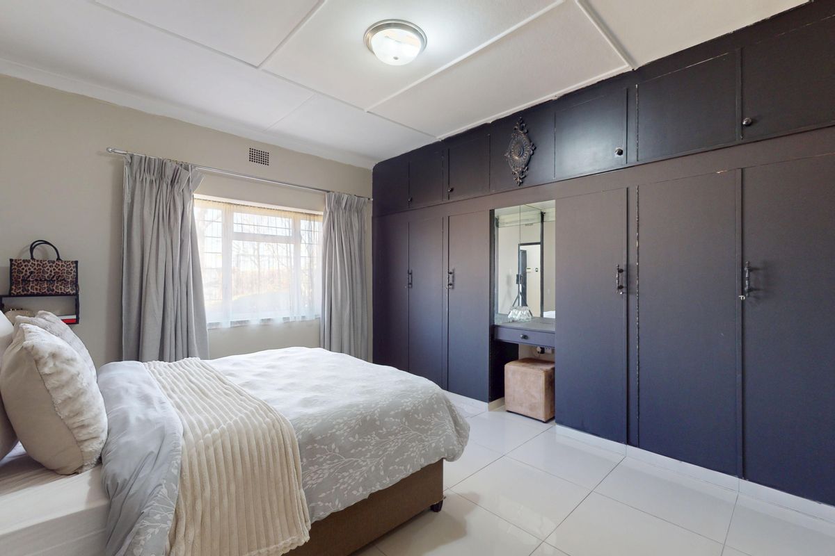 A well-maintained bedroom featuring extensive dark-toned built-in cabinetry with an integrated vanity mirror and bright tiled flooring.