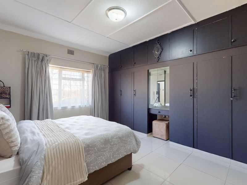 A well-maintained bedroom featuring extensive dark-toned built-in cabinetry with an integrated vanity mirror and bright tiled flooring.