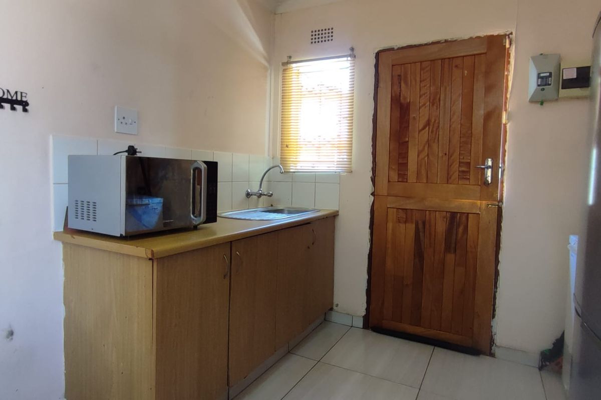 Compact kitchen area featuring timber cabinetry, a stainless steel sink, tiled splashback, and direct access via a timber door.