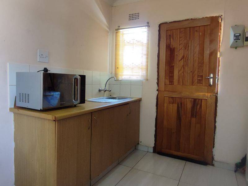 Compact kitchen area featuring timber cabinetry, a stainless steel sink, tiled splashback, and direct access via a timber door.