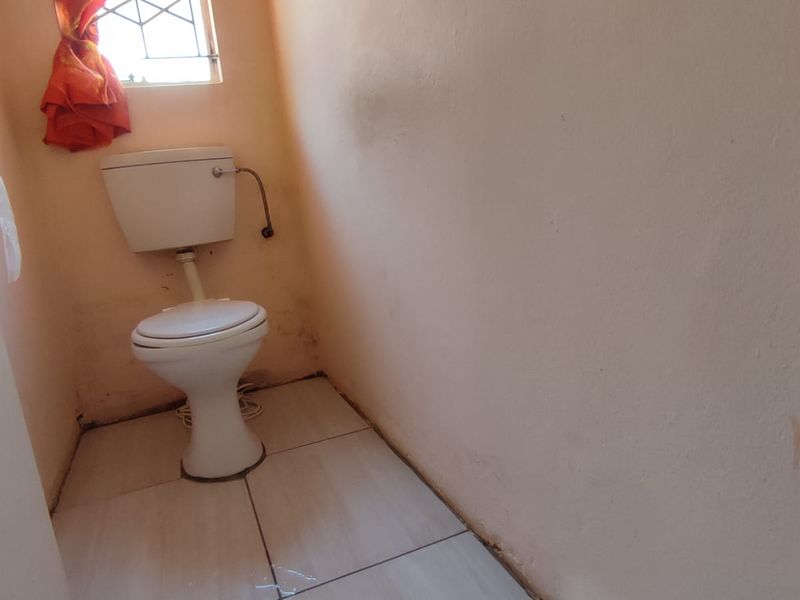 A small, functional bathroom featuring a standard toilet, tiled flooring, and a window with security bars, requiring cosmetic updates to improve its condition.