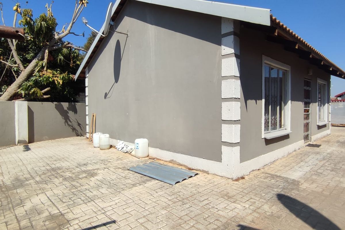 Rear exterior view of the property featuring paved ground, a security gate, and a satellite dish mounted on the side wall.
