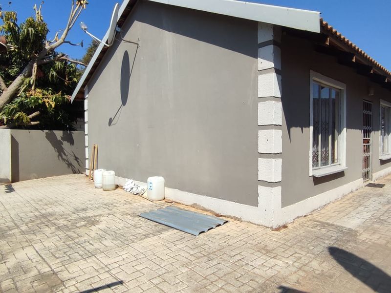 Rear exterior view of the property featuring paved ground, a security gate, and a satellite dish mounted on the side wall.