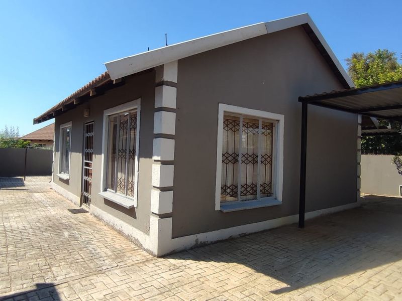 A detached house featuring a paved driveway, a carport, and security gates, set within a walled perimeter.