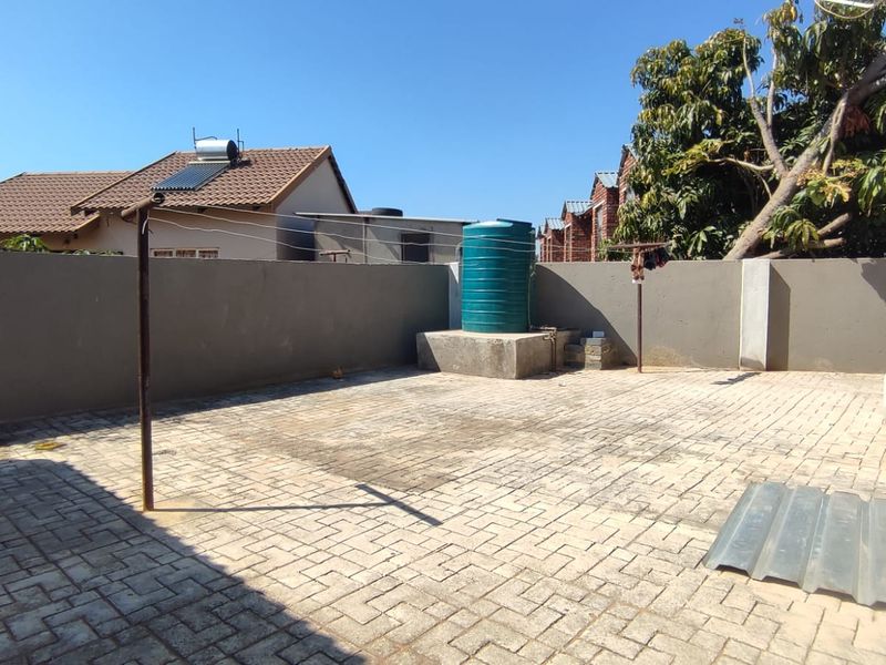 A paved rear courtyard featuring a perimeter wall, a water storage tank on a concrete plinth, and a fixed washing line.