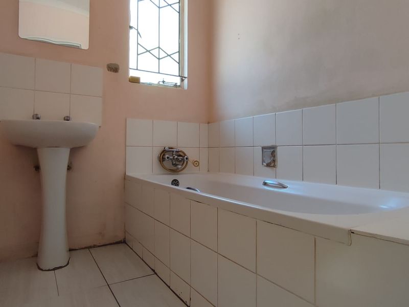 A functional bathroom featuring a pedestal basin and a tiled built-in bathtub, requiring cosmetic updates to improve its overall condition and appeal.