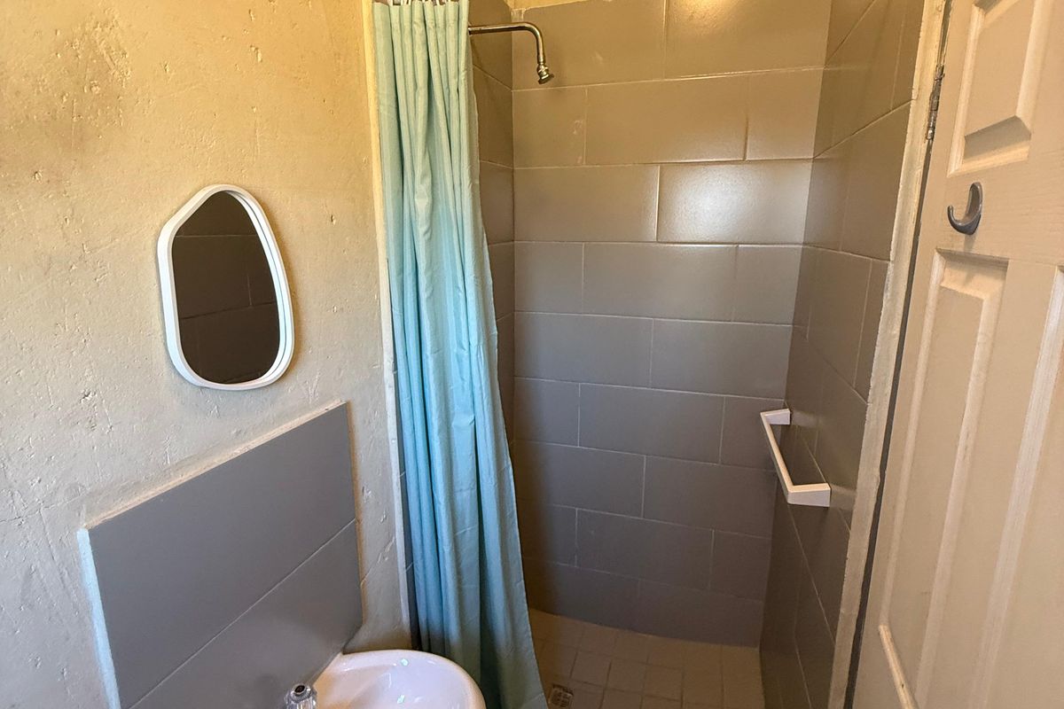 Compact bathroom featuring a pedestal washbasin and a tiled shower enclosure with a shower curtain.