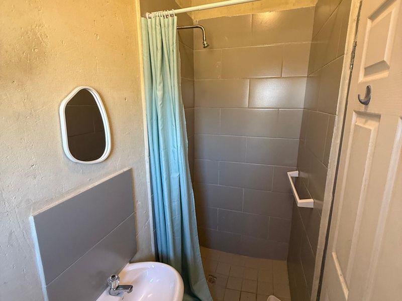 Compact bathroom featuring a pedestal washbasin and a tiled shower enclosure with a shower curtain.