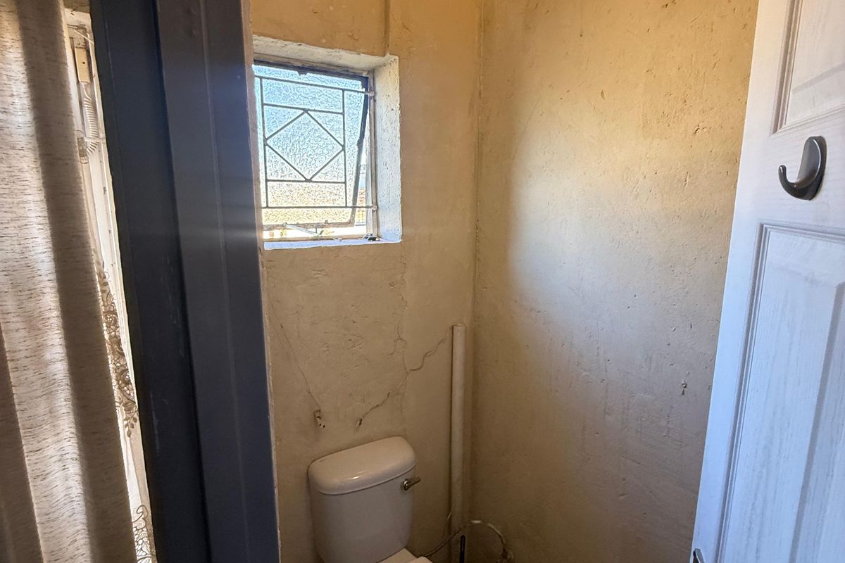 A small, dated bathroom featuring a toilet and leaded glass window, currently requiring significant cosmetic renovation and wall repairs.