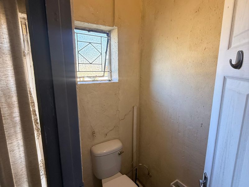 A small, dated bathroom featuring a toilet and leaded glass window, currently requiring significant cosmetic renovation and wall repairs.