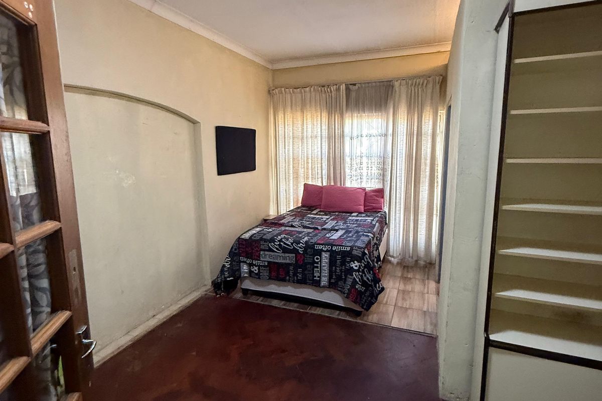 A bedroom featuring a built-in shelving unit, tiled flooring, and a timber door, offering a functional space with potential for cosmetic updates.