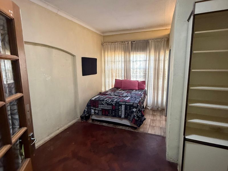 A bedroom featuring a built-in shelving unit, tiled flooring, and a timber door, offering a functional space with potential for cosmetic updates.