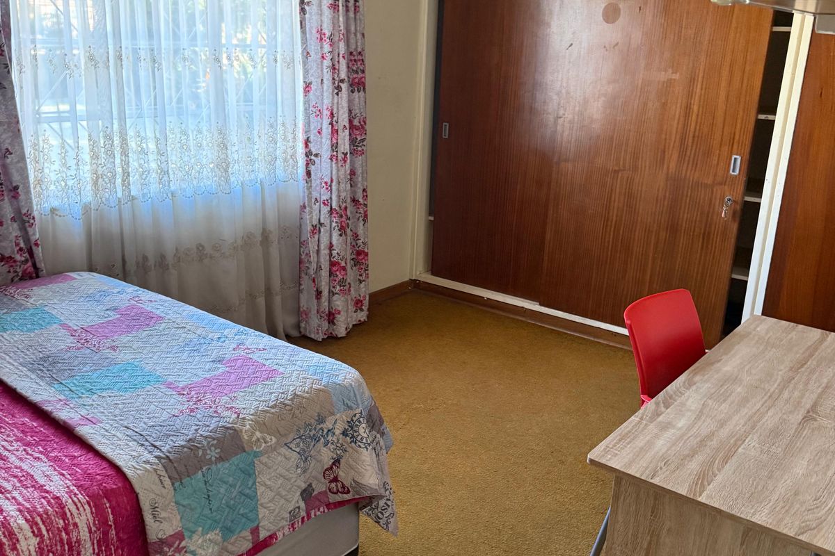 A bedroom featuring built-in wooden cupboards and carpeted flooring, offering a functional space with potential for modernization.