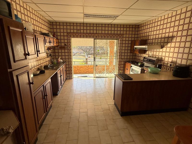 Spacious kitchen featuring dated wooden cabinetry, tiled walls and flooring, and direct access to an outdoor balcony area.