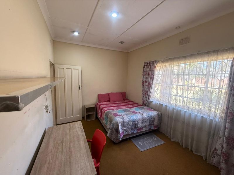 A bedroom featuring carpeted flooring, recessed ceiling lighting, and a window fitted with security bars, offering a functional space with potential for cosmetic updates.