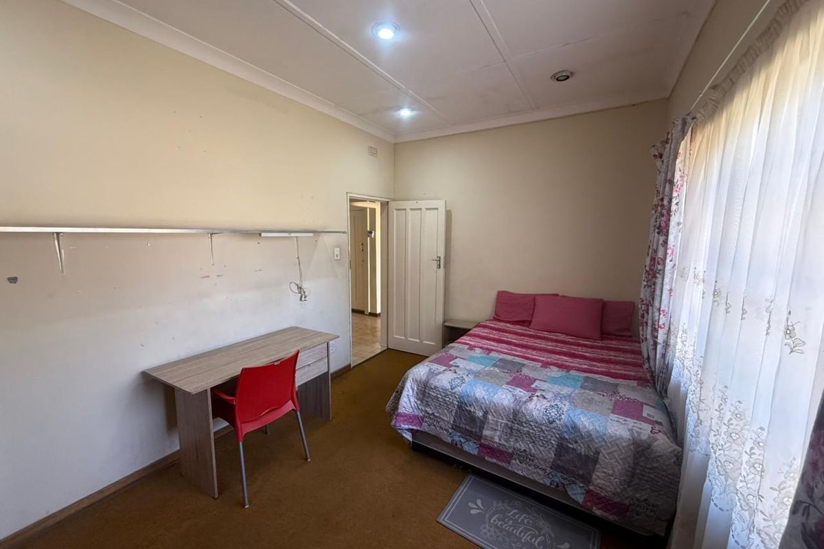 A functional bedroom featuring recessed downlighting, coved ceilings, and a wall-mounted shelf, with carpet flooring and access to an adjoining hallway.