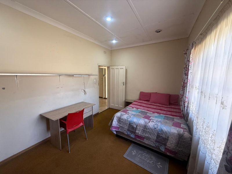 A functional bedroom featuring recessed downlighting, coved ceilings, and a wall-mounted shelf, with carpet flooring and access to an adjoining hallway.
