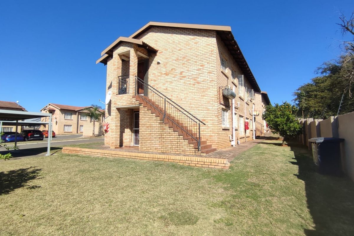 A view of the rear exterior of a face brick apartment building featuring an external staircase and surrounding lawn area.