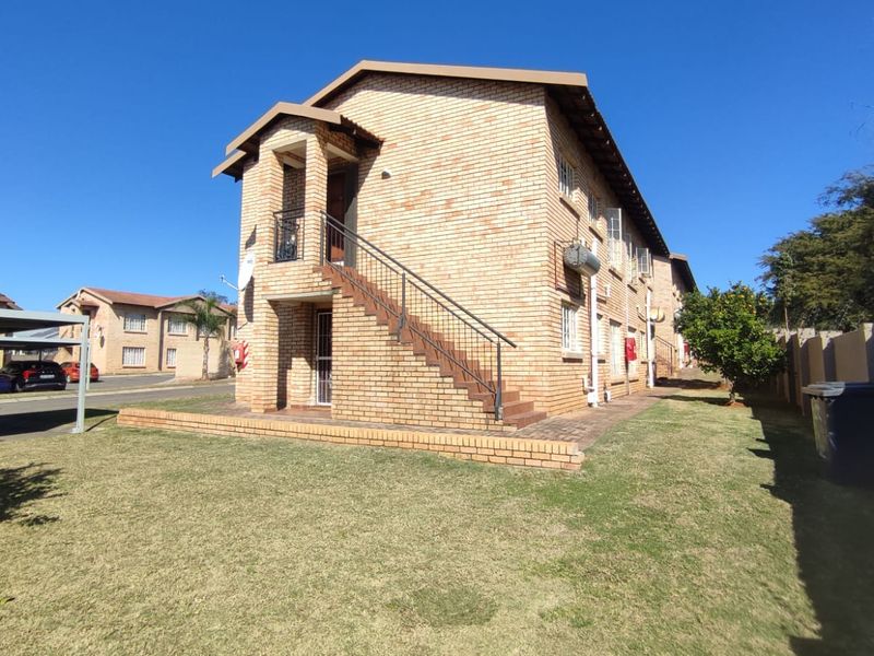 A view of the rear exterior of a face brick apartment building featuring an external staircase and surrounding lawn area.