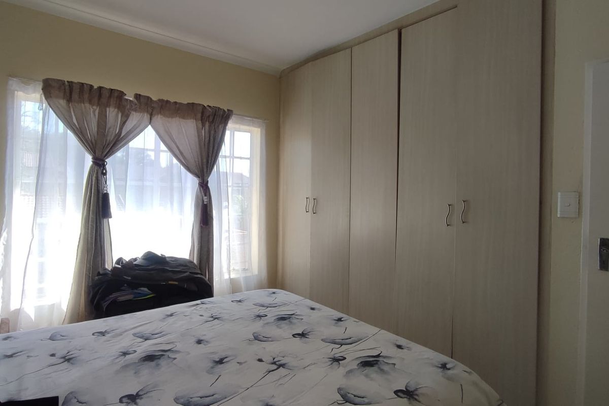 A bedroom featuring light-toned built-in cupboards and a window with security bars, providing functional storage and natural light.