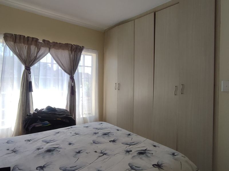 A bedroom featuring light-toned built-in cupboards and a window with security bars, providing functional storage and natural light.