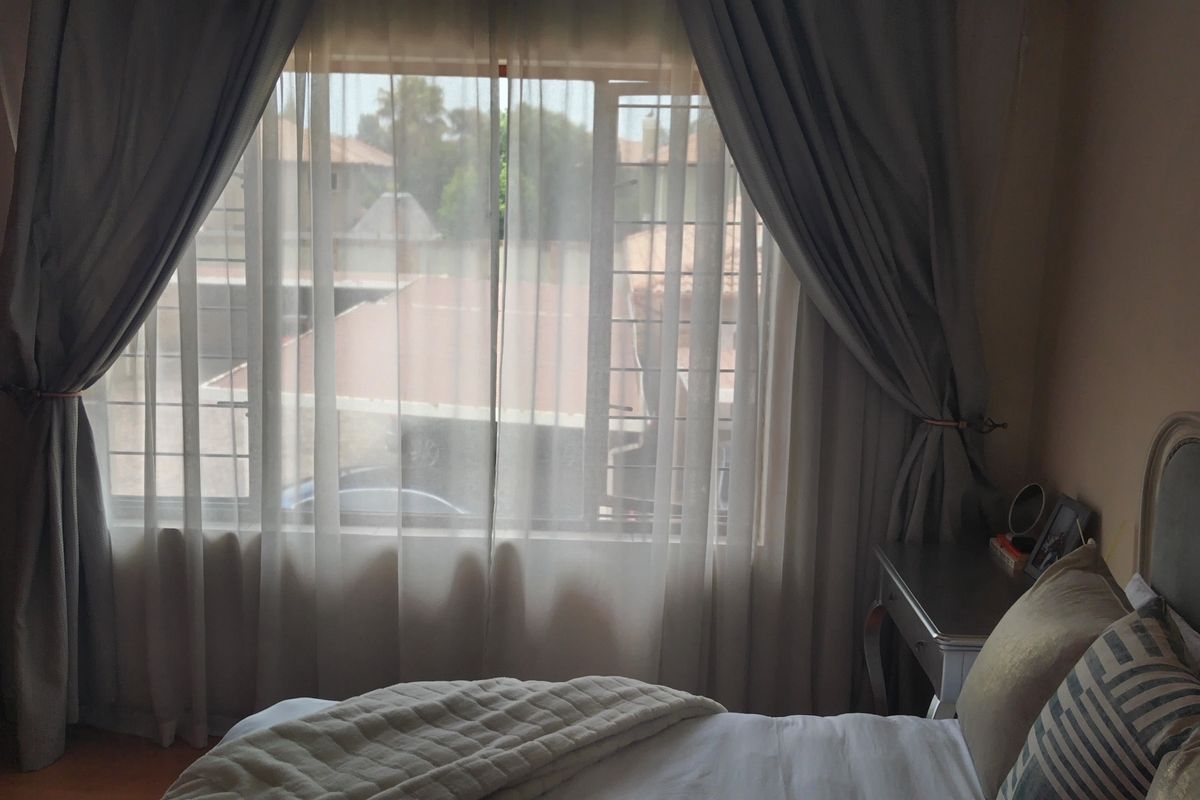 A bedroom featuring a built-in wardrobe and a window with security bars, offering natural light and a view of the surrounding area.