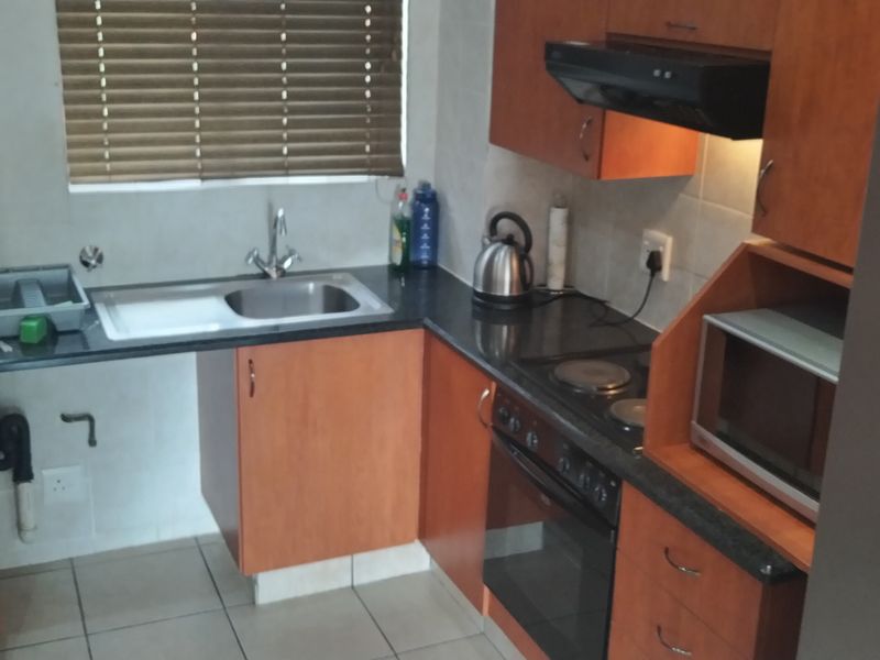 Compact kitchen featuring wood-finish cabinetry, dark countertops, built-in oven with hob, extractor fan, and tiled flooring.