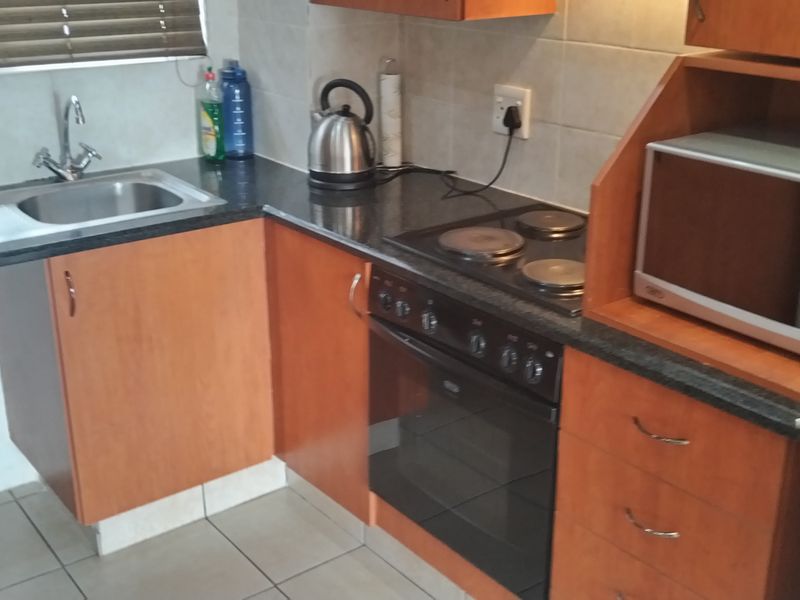A functional kitchen featuring laminate cabinetry, granite countertops, a built-in oven with electric hob, and a tiled backsplash.