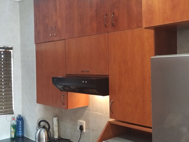 A functional kitchen featuring wooden cabinetry, a built-in extractor fan, tiled backsplash, and a sink area with a window.