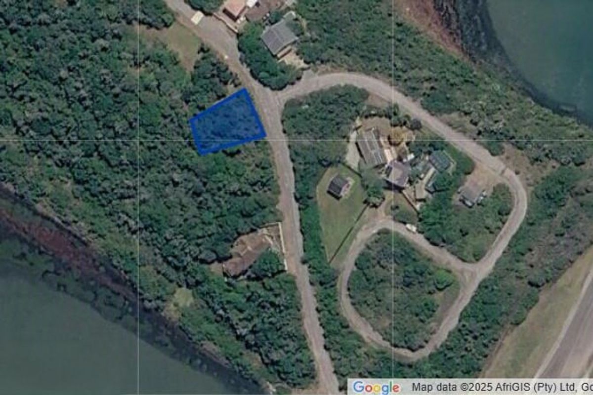 An aerial view showing a vacant residential plot surrounded by dense vegetation and nearby coastal water.
