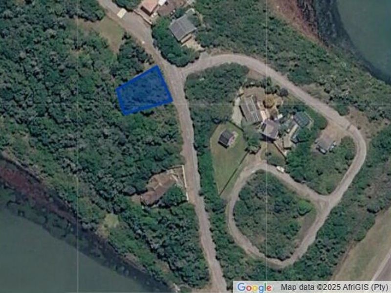 An aerial view showing a vacant residential plot surrounded by dense vegetation and nearby coastal water.