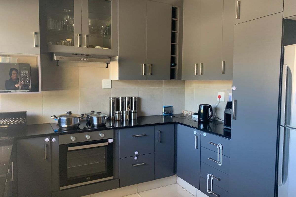 Modern kitchen featuring dark grey cabinetry, granite countertops, built-in oven, hob, and extractor fan with neutral tiled flooring and backsplash.