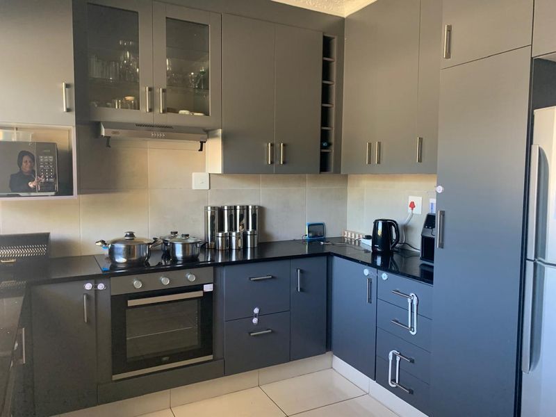Modern kitchen featuring dark grey cabinetry, granite countertops, built-in oven, hob, and extractor fan with neutral tiled flooring and backsplash.