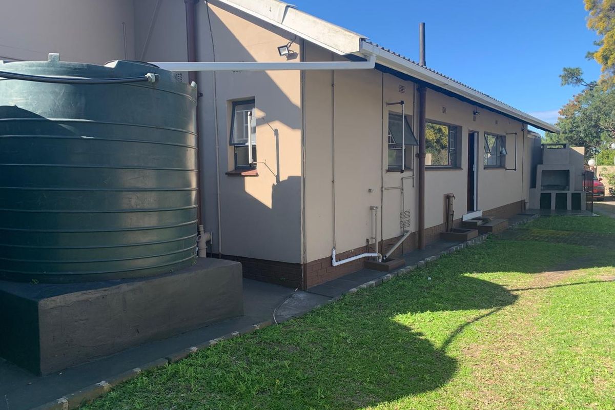 Rear exterior view of the house featuring a large water storage tank, built-in braai area, and well-maintained exterior walls and windows.