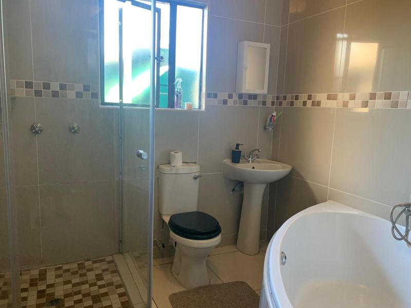 A functional bathroom featuring a pedestal basin, toilet, separate shower enclosure, and a bathtub with neutral wall and floor tiling.