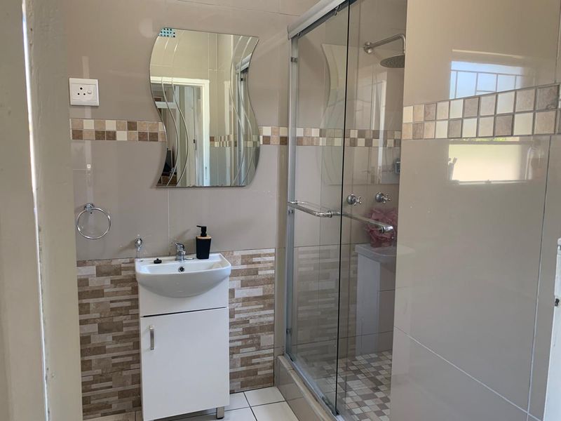 A modern bathroom featuring a vanity cabinet with a ceramic basin, a glass-enclosed shower, and neutral-toned wall and floor tiling.