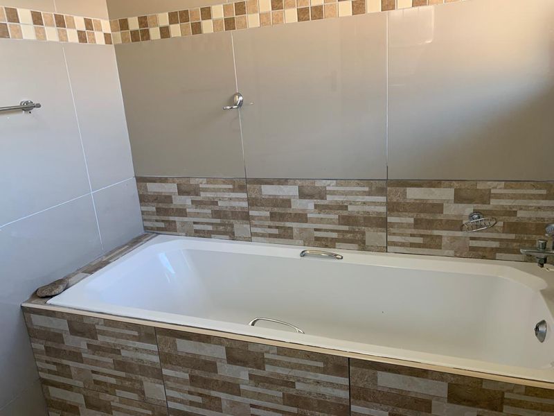 A clean bathroom featuring a built-in bathtub with decorative tiled surround and chrome fixtures.