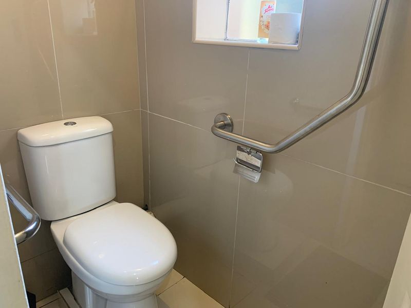 A functional bathroom featuring a modern toilet, tiled walls, and a stainless steel grab rail for accessibility.