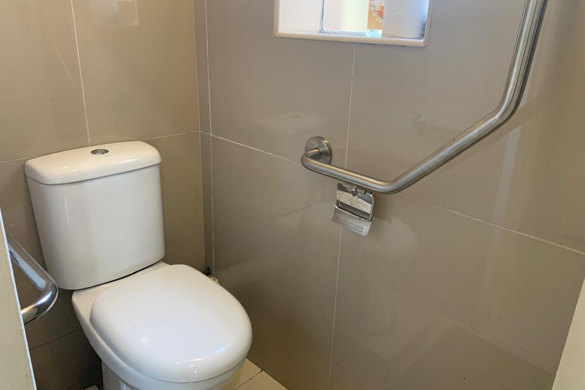 A functional bathroom featuring a modern toilet, tiled walls, and a stainless steel grab rail for accessibility.