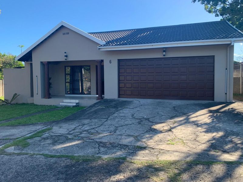 Front elevation of a single-story house featuring a double garage, covered entrance porch with decorative columns, and a concrete driveway.