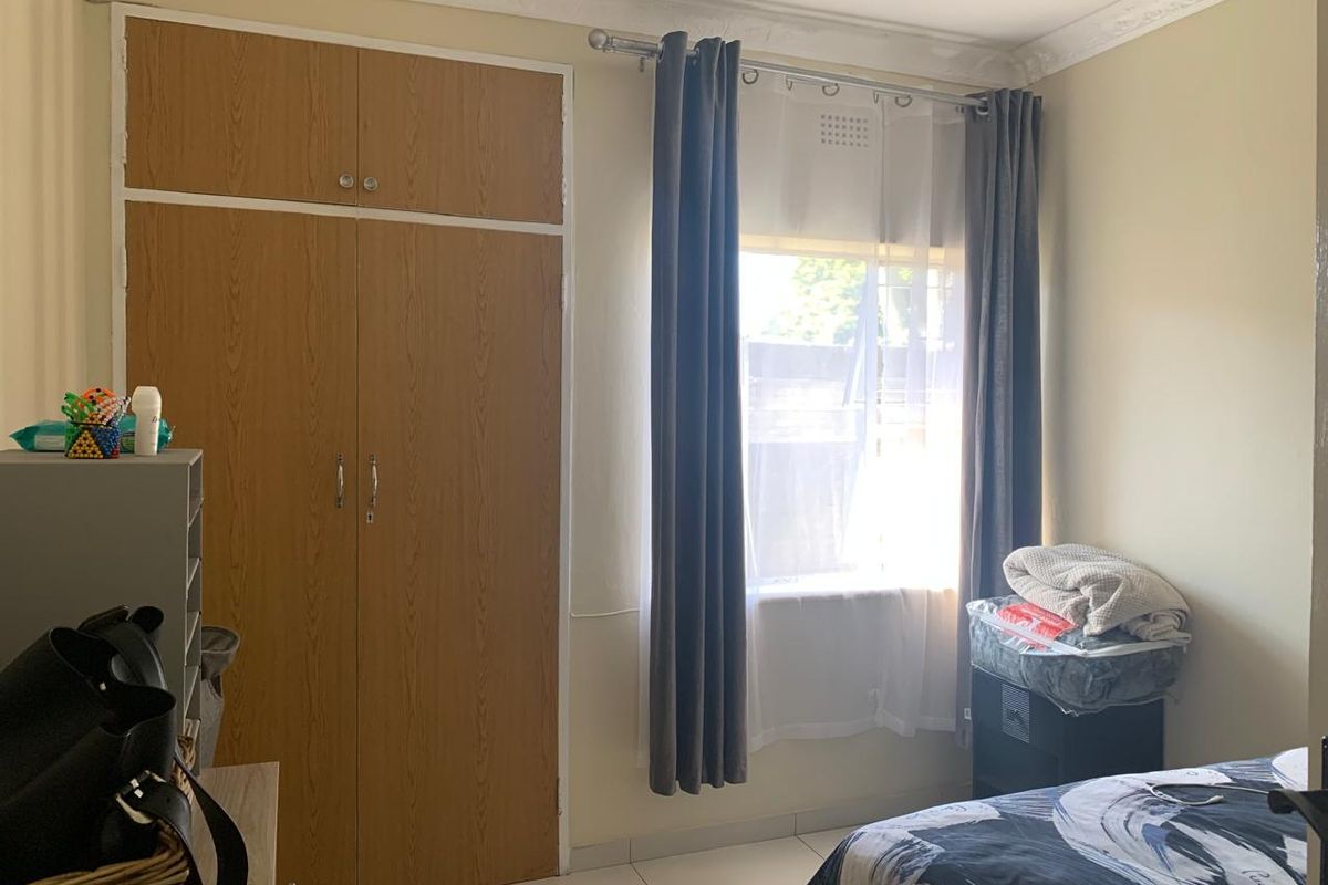 A bedroom featuring built-in wooden wardrobes, tiled flooring, and decorative ceiling cornicing, providing a functional and neutral living space.