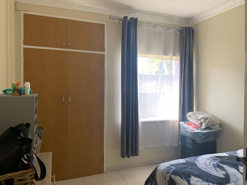 A bedroom featuring built-in wooden wardrobes, tiled flooring, and decorative ceiling cornicing, providing a functional and neutral living space.
