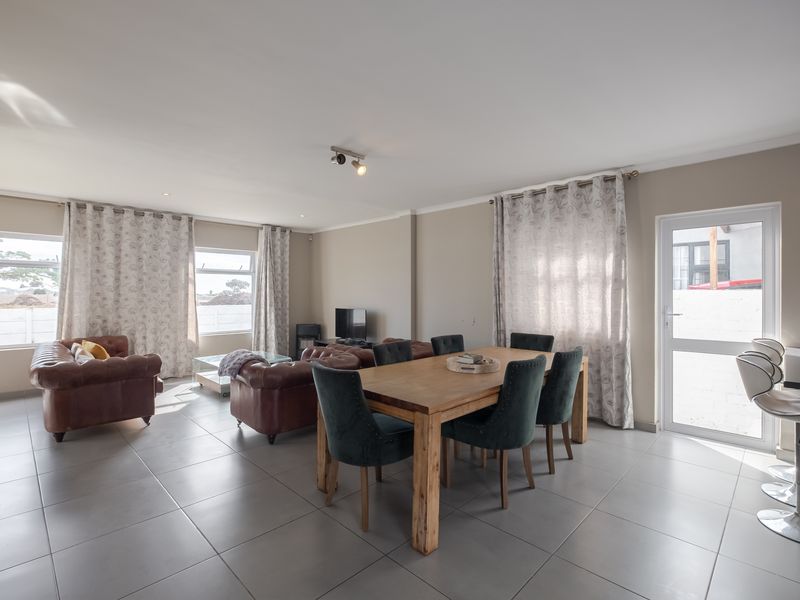 Spacious open-plan living and dining area featuring neutral tiled flooring, recessed lighting, and direct access to the exterior through a glass panel door.