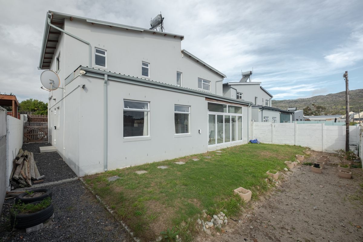 Rear view of the property featuring a multi-story facade, solar water heating system, sliding glass doors, and a private garden with perimeter walling.