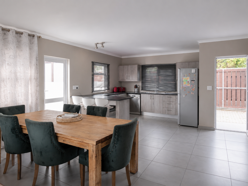 Open-plan kitchen and dining area featuring modern cabinetry, tiled flooring, and direct access to the exterior through a glass door.