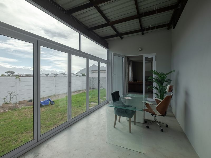 A bright, enclosed patio area featuring large aluminium sliding doors, exposed steel roof beams, and polished concrete flooring, overlooking the rear garden.