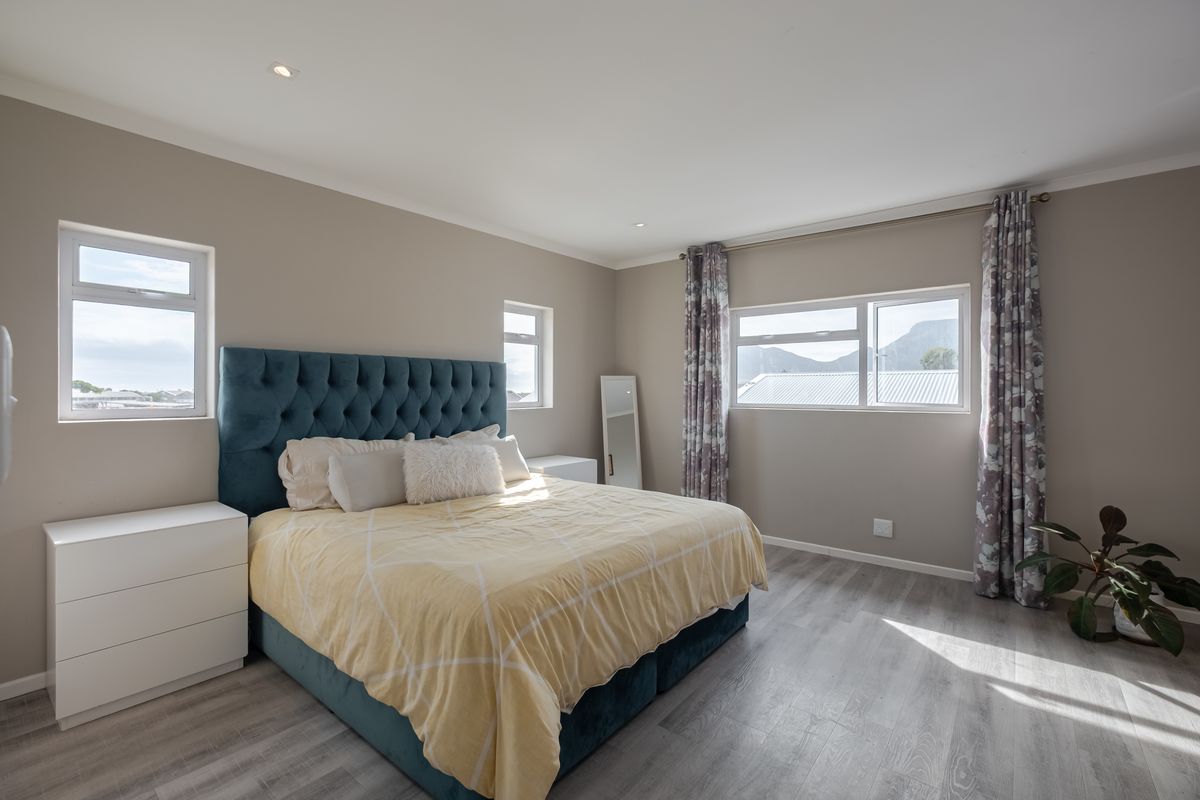 A bright and spacious bedroom featuring modern laminate flooring, recessed downlighting, and multiple windows providing natural light and mountain views.