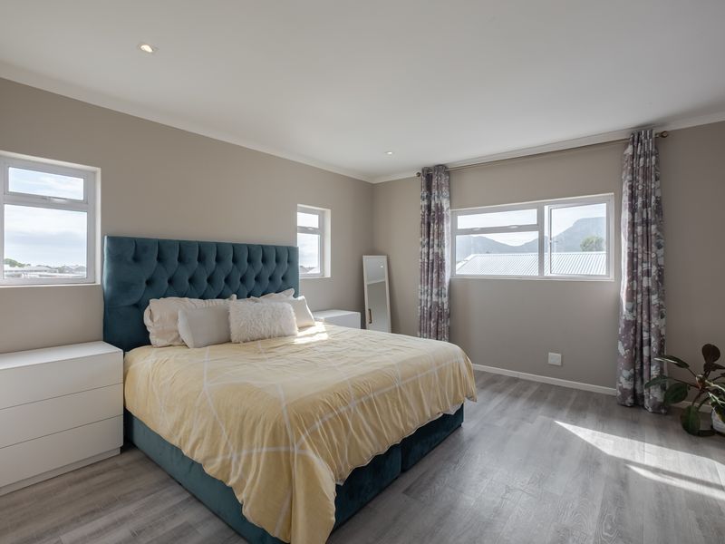 A bright and spacious bedroom featuring modern laminate flooring, recessed downlighting, and multiple windows providing natural light and mountain views.